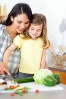 Adorable little girl cutting vegetables with her mother in the kitchen